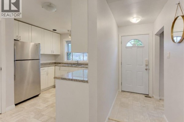 View of the kitchen and front entryway. Kitchen has stainless steel appliances and white cabinets. - 174 Glen Road, Kitchener