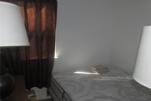 Bedroom with a single mattress, brown curtains, and two lamps. - 1742 Quebec Street, Regina