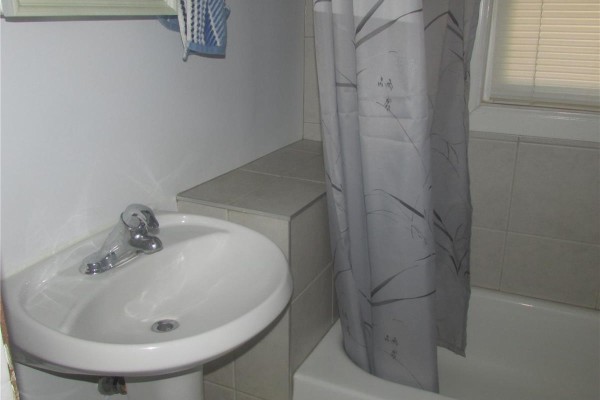 Bathroom with a white sink, grey tiled walls, and a bathtub with a shower curtain. - 1742 Quebec Street, Regina