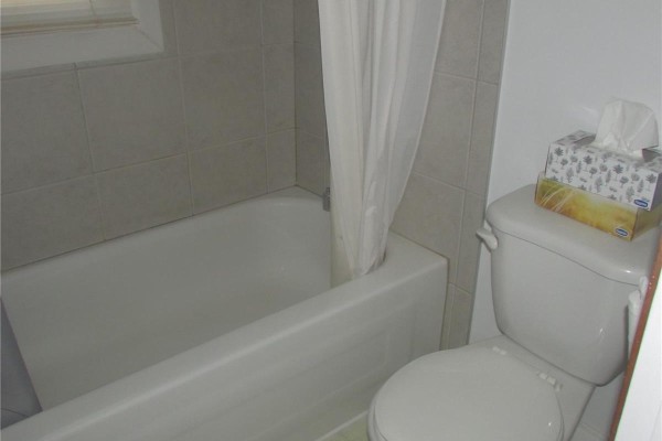 Bathroom with a white bathtub and toilet, featuring a grey shower curtain and tissue box. - 1742 Quebec Street, Regina
