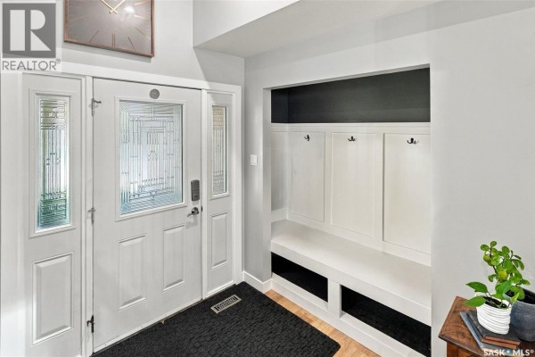 White front door with glass panels and a built-in entryway storage bench. - 1743 Blair Bay E, Regina