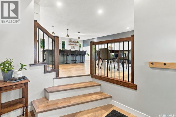 Stairs with wood treads and black railings leading to an open-concept kitchen and dining area. - 1743 Blair Bay E, Regina