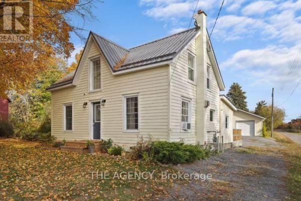 Side view of a yellow siding house with a metal roof and a detached garage. - 12 - 1743 County Road, Prince Edward County