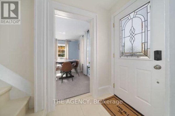 Interior view of a house foyer showing a white door with stained glass and a doorway to a dining area. - 12 - 1743 County Road, Prince Edward County