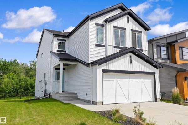 Side exterior view of a modern white house with black trim and a prominent two-car garage. - 17431 7 St Ne, Edmonton