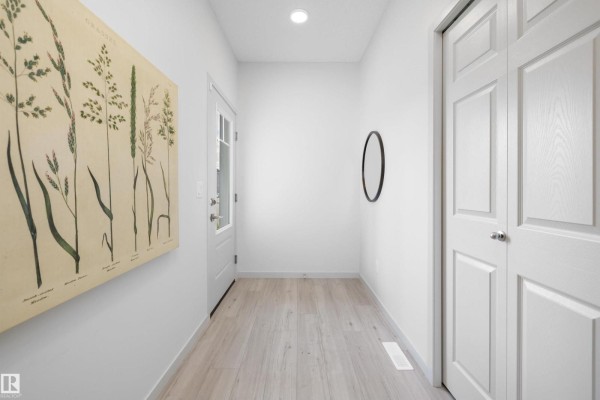 Entrance hallway with light wood laminate flooring, white walls, and double bi-fold closet doors. - 17431 7 St Ne, Edmonton