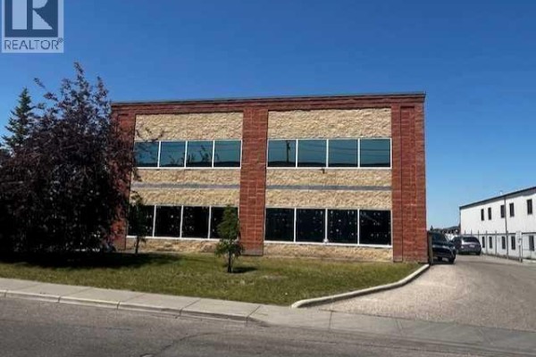 Side exterior of a commercial building with tan stone, red brick accents, and large windows. - 175, 5120 47 Street Ne, Calgary