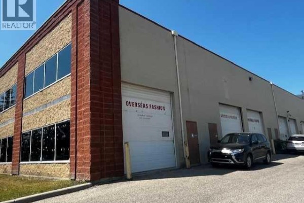 Rear exterior of a commercial building showing loading bay doors, windows, and parked vehicles. - 175, 5120 47 Street Ne, Calgary