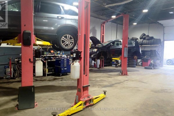 Auto repair bay with two red car lifts, multiple vehicles, tires stacked, and equipment. - 175 Limestone Crescent, Toronto