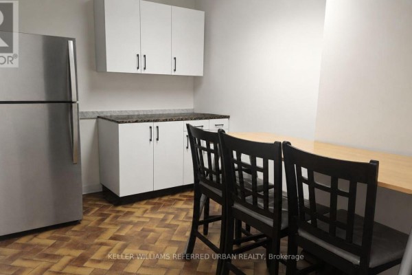 Small kitchen area with a stainless steel refrigerator, white cabinets, and a wooden table with chairs. - 175 Limestone Crescent, Toronto