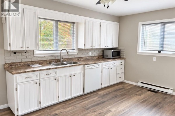 View of the backyard with a detached garage, paved area, and a screened-in porch on the house. - 175 Second Avenue, Moncton