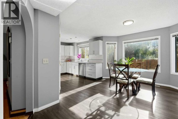 Open concept kitchen and dining area with white cabinets, stainless steel appliances, and large windows. - 175 Shannon Circle Sw, Calgary