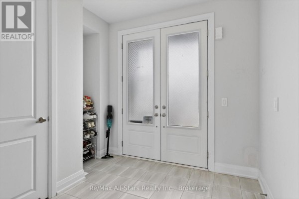The interior entryway with tiled flooring, double glass doors, and a shoe rack with a vacuum cleaner. - 175 St. Joseph Road, Kawartha Lakes