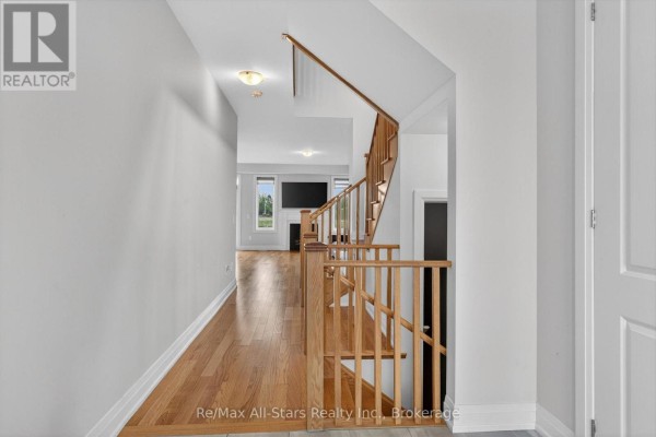 A hallway with hardwood floors, a wooden staircase with black railings, leading to an open living area. - 175 St. Joseph Road, Kawartha Lakes