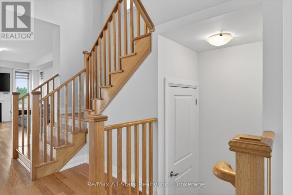 A close-up of a wooden staircase with light wooden railings and treads, leading to a second floor hallway. - 175 St. Joseph Road, Kawartha Lakes