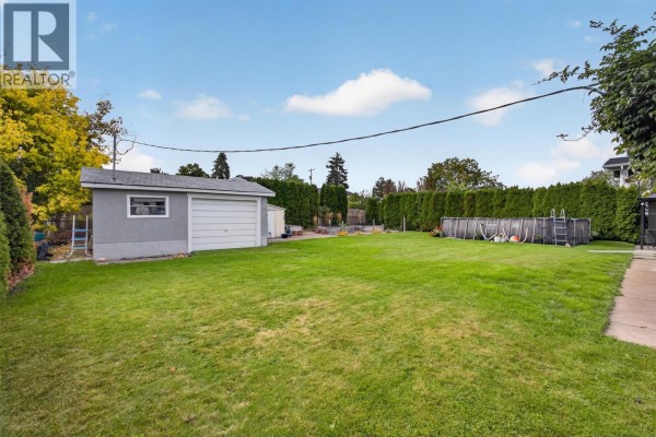 Backyard with a large green lawn, an above-ground pool, and a detached garage. - 175 Venus Road, Kelowna