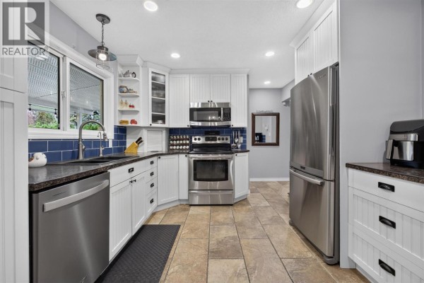 Modern white kitchen with stainless steel appliances, granite countertops, and blue tile backsplash. - 175 Venus Road, Kelowna