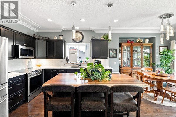 Kitchen with black cabinets, white quartz countertops, and a large wooden island. - 1752 White Blossom Way, Nanaimo