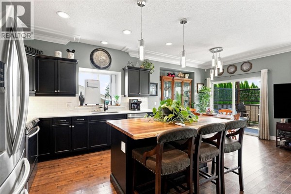 View of the kitchen, dining area, and sliding glass doors leading to an outdoor patio. - 1752 White Blossom Way, Nanaimo