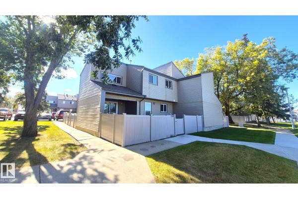 Corner view of the townhouse exterior with a sidewalk, grass, trees, and vehicles parked nearby. - 1754 Lakewood Rd S Nw, Edmonton