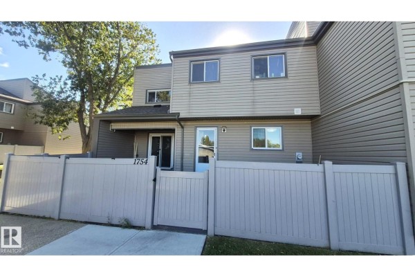 View of the townhouse front with a light grey fence, two doors, and windows on two levels. - 1754 Lakewood Rd S Nw, Edmonton