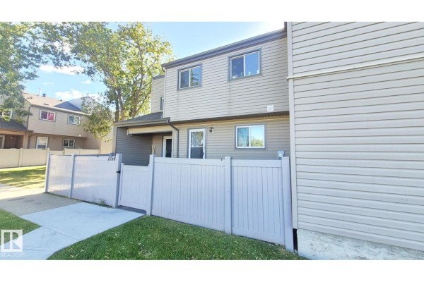 Side exterior view of the townhouse showing beige siding, windows, and a portion of the fence. - 1754 Lakewood Rd S Nw, Edmonton