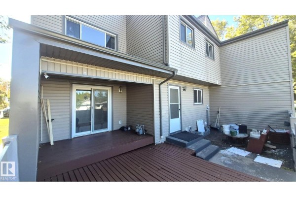 Rear exterior of the townhouse featuring a wooden deck, two doors, steps, and storage items. - 1754 Lakewood Rd S Nw, Edmonton