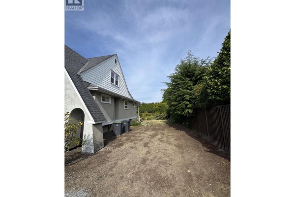 Gravel driveway next to a stucco house with mature trees and a dark fence. - 1758b Western Parkway, Vancouver