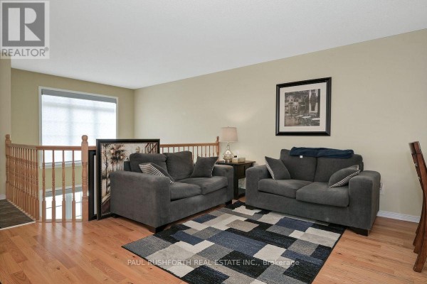 Living room with two grey sofas, a patterned rug, wooden floors, and a large window. - 176 - 70 Edenvale Drive, Ottawa