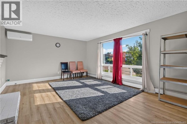 Living room with light wood floors, grey rug, and a large window with red curtains and exterior view. - 176-178 Ayer Avenue, Moncton