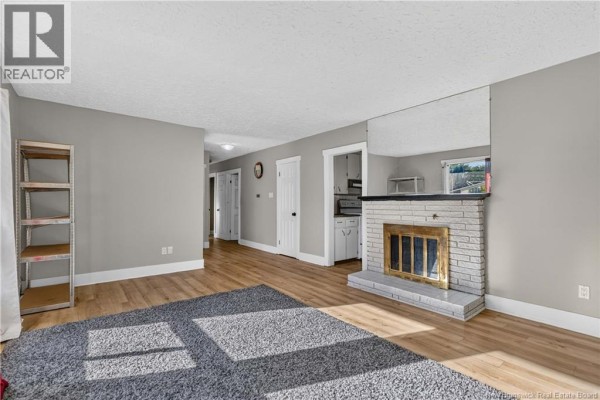 Living room with a brick fireplace, wood floors, a grey rug, and a hallway leading to other rooms. - 176-178 Ayer Avenue, Moncton