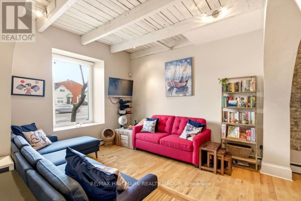 Living room with a sectional sofa, bright pink sofa, wood floors, and exposed white ceiling beams. - 176 King Edward Avenue, Ottawa