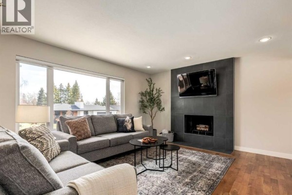 Living room with a sectional sofa, a fireplace with a mounted TV, and large windows. - 176 Mapleburn Drive Se, Calgary