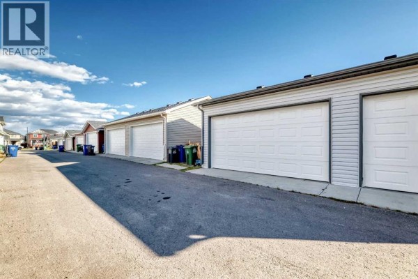 Back alley view of a row of attached garages with white doors. - 176 Willow Park, Cochrane