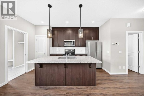 Kitchen with dark wood cabinets, granite island, stainless steel appliances, and wood floors. - 176 Willow Park, Cochrane