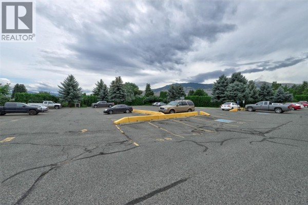 A paved parking lot with yellow barriers and a view of hills. - 1760 Brunner Avenue Unit# 218, Kamloops