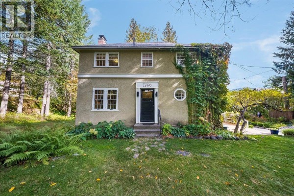Front view of a stucco two-story house with a black front door and decorative window. - 1760 Park Street, Rossland