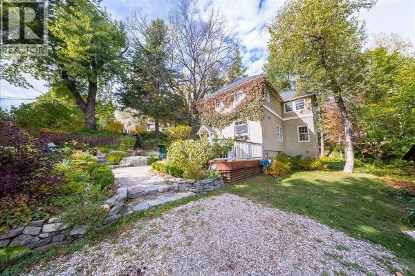 Rear view of a stucco house with a wooden deck and stone pathways in a terraced garden. - 1760 Park Street, Rossland