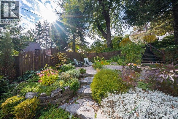 Stone pathway leading through a lush garden with outdoor seating and mature trees. - 1760 Park Street, Rossland
