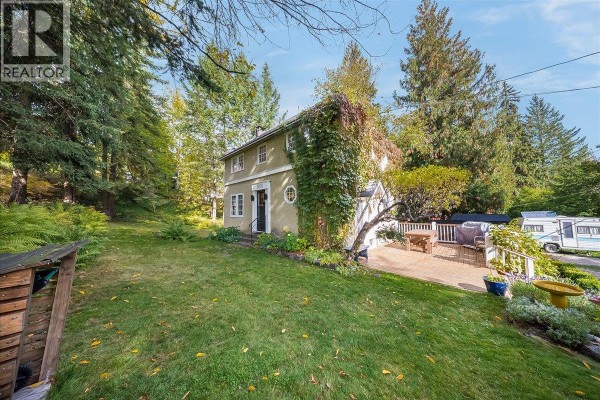 View of a stucco house, wooden deck, and grassy yard from the side with surrounding trees. - 1760 Park Street, Rossland