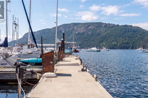 Concrete dock with boats moored on the left and a forested hill view. - 1765 Cowichan Bay Rd, Duncan