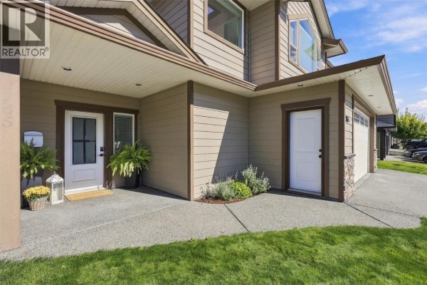 Close-up of the house exterior showing the front door, garage door, and beige siding. - 1765 Foxtail Drive, Kamloops