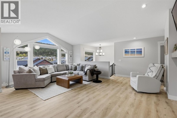 Spacious living room with a large sectional sofa, brown leather ottoman, and expansive windows with a view. - 1765 Foxtail Drive, Kamloops