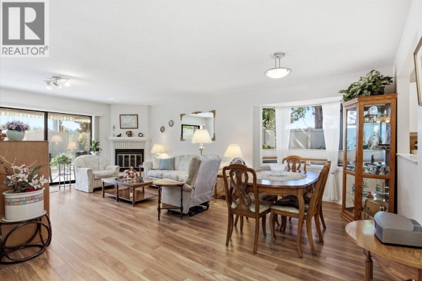 Spacious living and dining area with a fireplace, bay window, wooden floors, and dining table with chairs. - 1765 Leckie Road Unit# 201, Kelowna