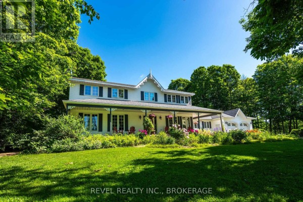 Side view of white farmhouse with wrap-around porch and detached three-car garage on gravel drive. - 1766 Hitchcock Drive, South Frontenac