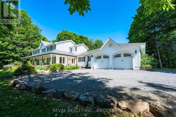 Front view of white farmhouse with wrap-around porch, red Adirondack chairs, and spring flowers. - 1766 Hitchcock Drive, South Frontenac