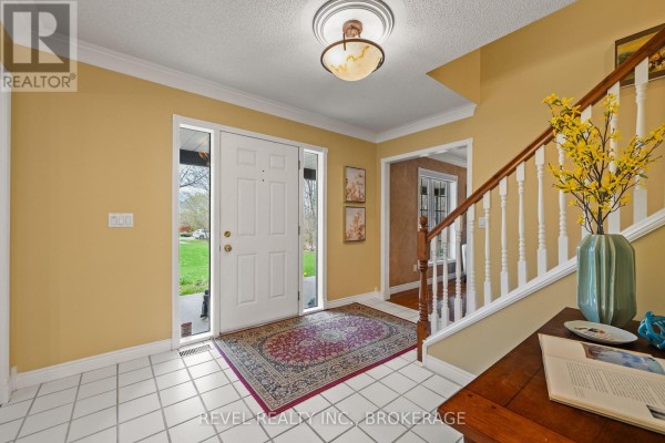 Interior foyer with white tile floor, red patterned rug, white front door, and wooden staircase. - 1766 Hitchcock Drive, South Frontenac