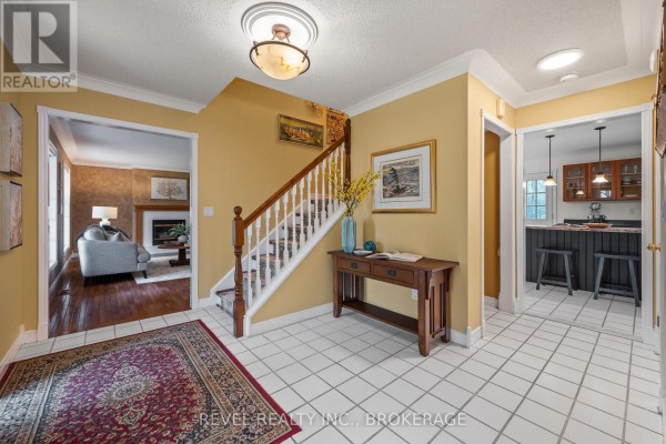 Interior foyer connecting to living room with fireplace and kitchen with island and stools. - 1766 Hitchcock Drive, South Frontenac