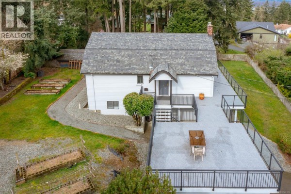 White house with a large deck, arched windows, and a stone chimney. - 1766 Pritchard Rd, Cowichan Bay