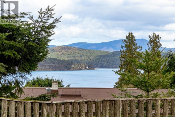 View of boats docked in Cowichan Bay from the property, framed by trees. - 1766 Pritchard Rd, Cowichan Bay